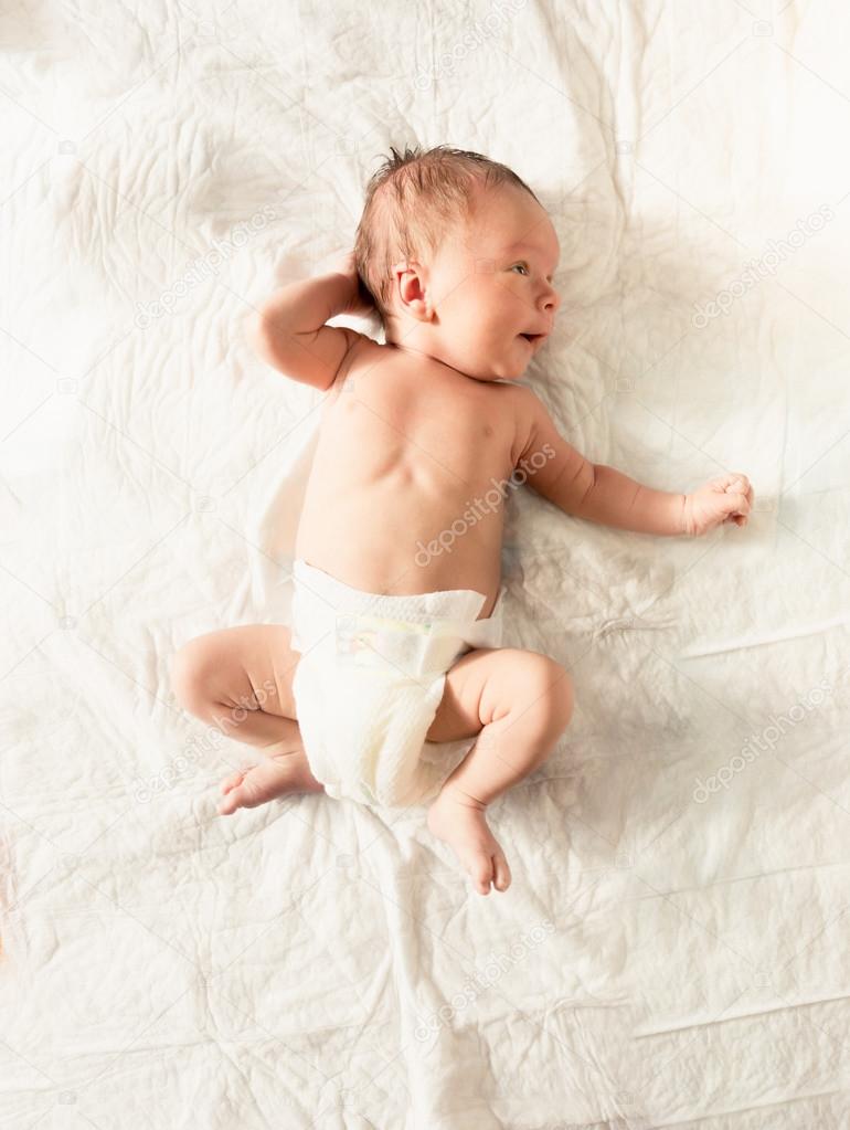 Cute newborn baby in diapers lying on white sheets on bed