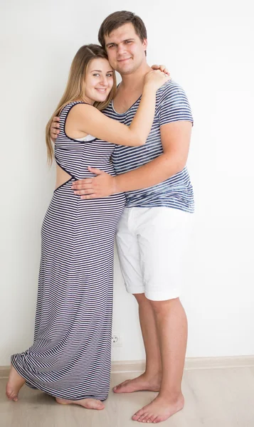 Couple enceinte en vêtements rayés posant contre le mur blanc — Photo