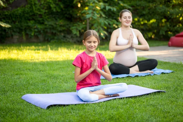 Mujer embarazada joven y linda chica practicando yoga en el parque — Foto de Stock