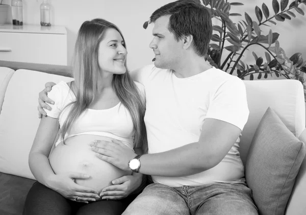 Černobílý portrét šťastné těhotné dvojice sedící na sof — Stock fotografie