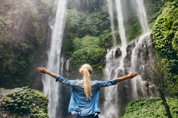 Woman standing by waterfall with her hands raised — Stock Photo, Image