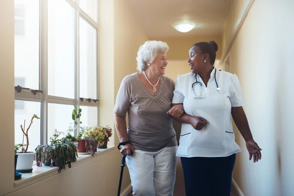 Smiling healthcare worker and senior woman walking together Stock Photo