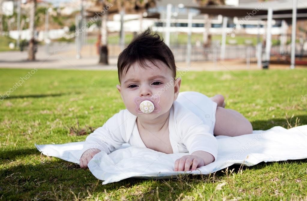 Charming baby girl with dummy lying on a green grass