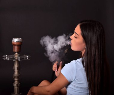 Kız siyah arka planda nargile içiyor. Duman ağızdan çıkar. Sigara içmenin zevki