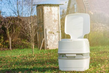 Sokak lambası. Ön planda taşınabilir plastik bir tuvalet. Arka planda kırık kapılı ahşap bir sokak tuvaleti var.