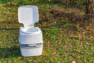 Sokak lambası. Ön planda taşınabilir plastik bir tuvalet. Arkada bir ağaç var.