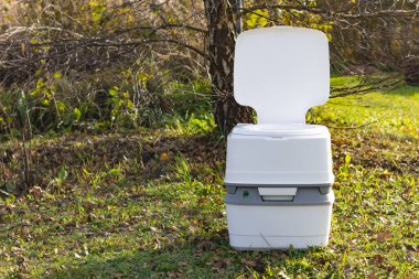 Sokak lambası. Ön planda taşınabilir plastik bir tuvalet. Arkada bir ağaç var.