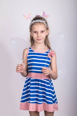 Stüdyo ışıkları. Okul çağındaki bir kız bize bakıp gülümsüyor. Arkasında kelebek kanatları var. Yakın plan..