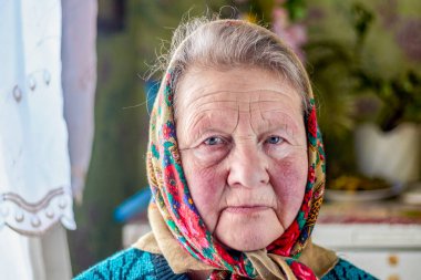 Ev ortamı. Yaşlı bir kadın. O, kafasında bir başörtüsüyle kötü bir şekilde giyinmiş. Arkasında retro tarzı bir gardırop var. Yakın plan. Para yok..