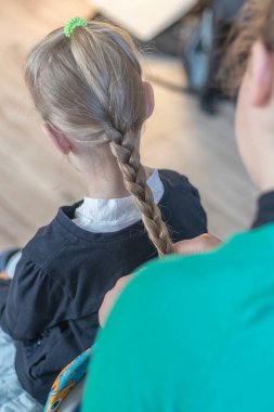 Sandalyedeki kız arkası bize dönük oturuyor. Yetişkin bir insan elleriyle saçlarını uçurur. Yakın plan.,