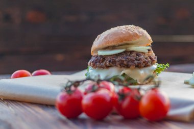 Burger evde yaptı. Onun yanında bir dalda kırmızı domatesler var. Yakın plan.