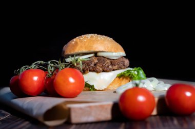 Burger evde yaptı. Onun yanında bir dalda kırmızı domatesler var. Yakın plan.