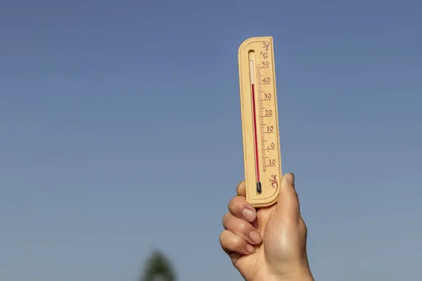 Natural lighting. a human hand holds a wooden thermometer. The temperature on it is very high. Heat