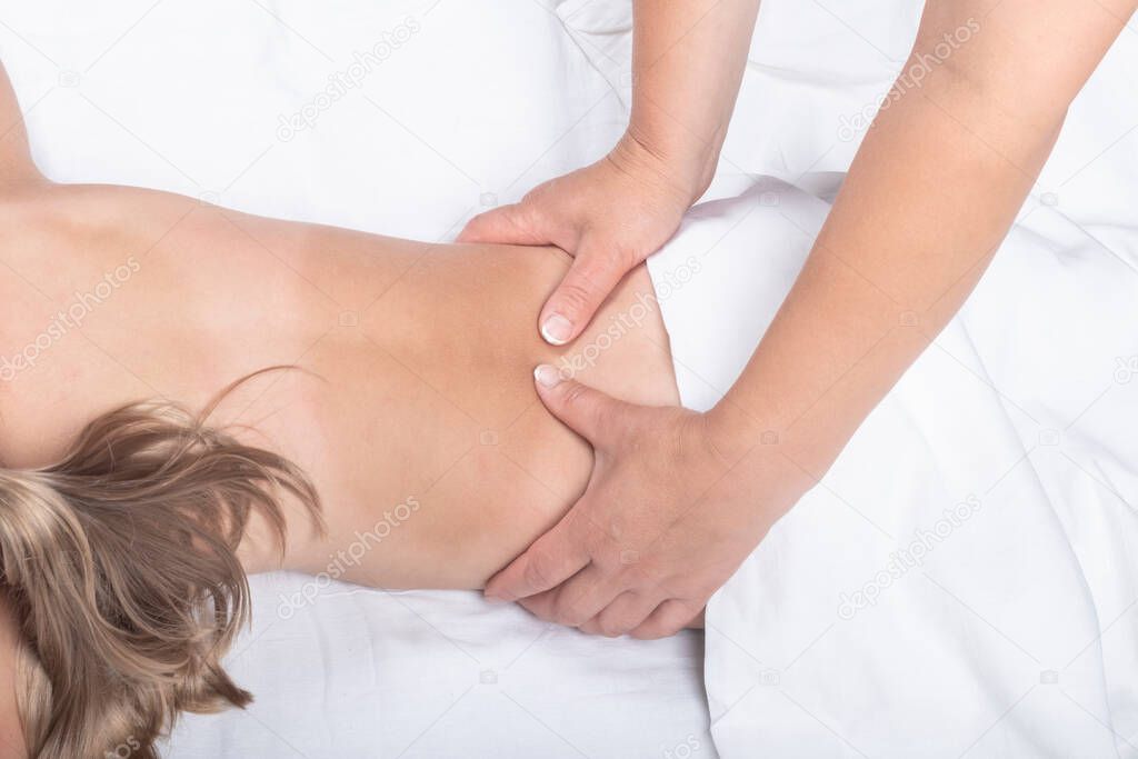 A teenage girl with white hair is lying on her stomach. A professional doctor does a back massage. Close-up