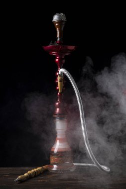 Yakın plan. Cam mataralı nargile ve metal kaseli nargile dumanı var. Siyah arka plan. Ön görünüm
