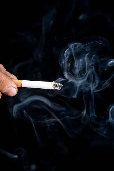 黑色背景 一个皮肤粗糙的人的手拿着一支香烟 蓝色的烟是从那里冒出来的 特写镜头 — 图库照片