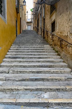 Taş duvarlar arasında parmaklıklar olan dar taş merdivenler.