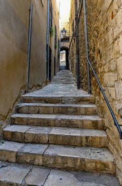 Taş duvarlar arasında parmaklıklar olan dar taş merdivenler.