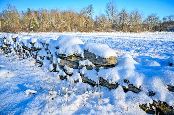 Muro de piedra cubierto de nieve cerca del campo agrícola — Foto de Stock