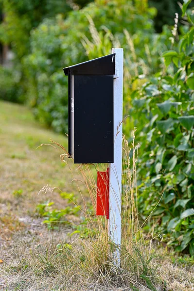 Schwarzer Briefkasten auf weißem Holzpfahl in Heckennähe — Stockfoto