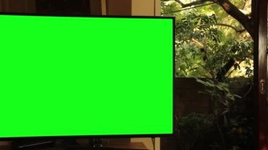 Oturma odasında yeşil ekranlı akıllı televizyon. Yakınlaştır. Yeşil ekranı istediğin görüntüyle ya da resimle değiştirebilirsin. Sonraki Efektler ya da herhangi bir video düzenleme yazılımında Keying efekti ile yapabilirsiniz (YouTube 'daki derslere bakın).  