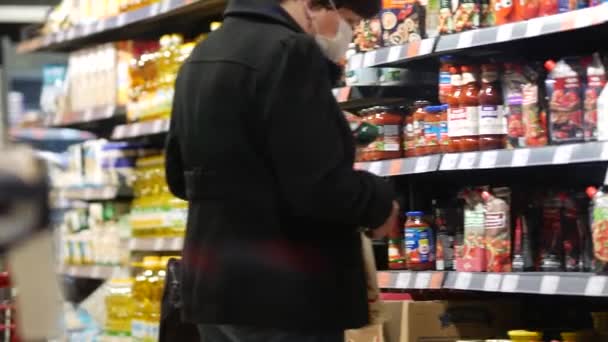 Mujer de mediana edad con máscara de protección en la cara elige comestibles en el supermercado. — Vídeo de stock