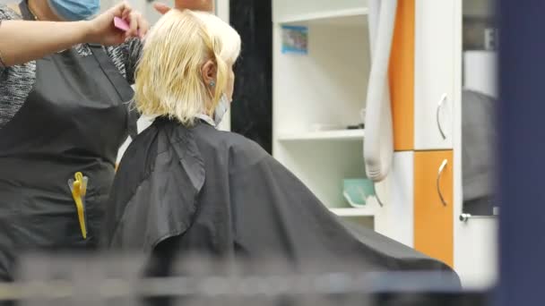 Coiffeur en masque facial coupe les cheveux de la femme le soir. blonde dans la chaise de coiffeur — Video