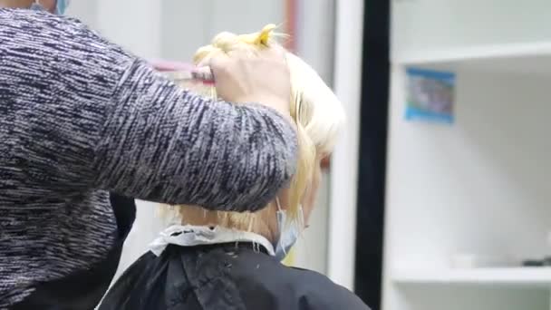 Fryzjer w masce do twarzy strzyże kobiety wieczorem. blondynka w fotelu fryzjerskim — Wideo stockowe