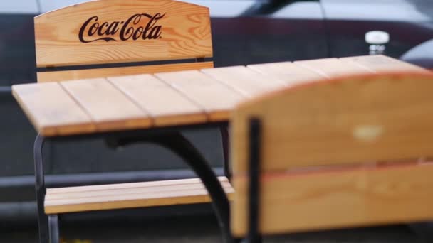 Trä bord och stolar i en gata café med Coca Cola logotyp tillämpas. CocaCola Ordförande — Stockvideo