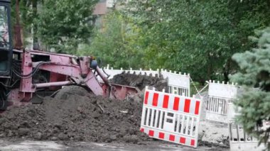 Bir traktör bir şehir caddesindeki hendeği dolduruyor. Plastikten yapılmış güvenlik çiti