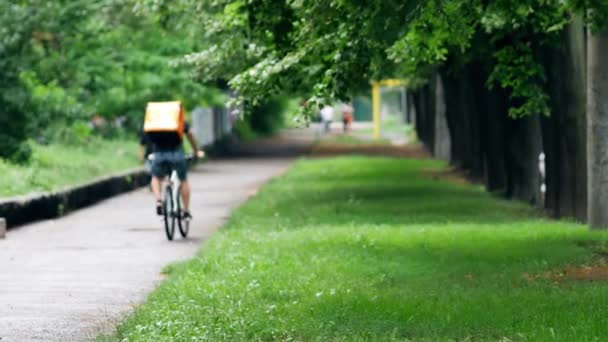 Un mensajero de reparto con una mochila Raketa naranja de marca monta en bicicleta — Vídeos de Stock