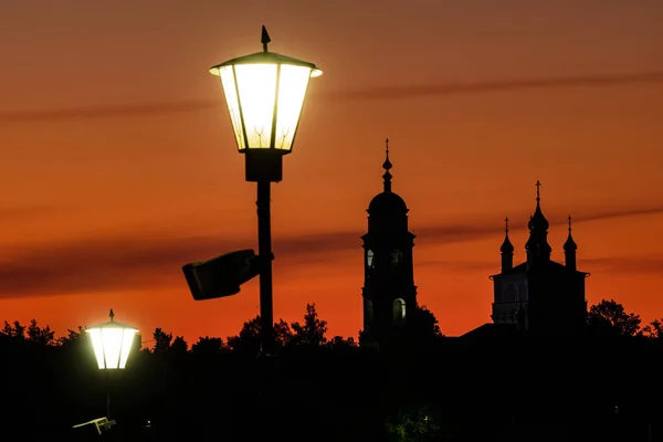 Silhuetten av en ortodox kyrka mot bakgrund av en skinande guld ljus orange himmel. — Stockfoto
