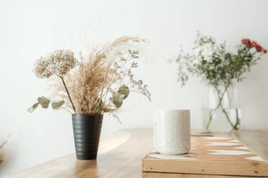 Vazolarda kurumuş çimenler beyaz bir masada duruyor..