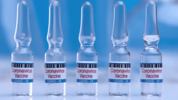 Vaccin contre le coronavirus en ampoules gros plan sur fond bleu de table de laboratoire. Médicaments pharmacologiques contre la pandémie Covid-19. Vaccin médical contre le danger mondial 2019-ncov. — Video