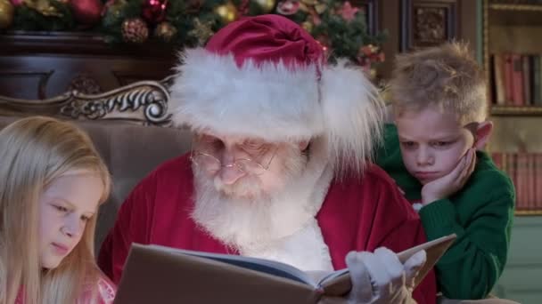 Santa čte knížku malým dětem, z knihy září jasné magické světlo. Šťastné děti poslouchají vánoční příběh od Santa Clause. Veselé Vánoce a šťastný Nový rok. Zázraky času.