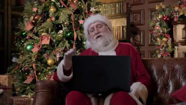 Santa Claus v sociální vzdálenosti v covid19 pandemie sedí doma s notebookem, komunikovat prostřednictvím videa a chatu. Šťastný Santa volá přes video odkaz a přeje všem veselé Vánoce a Nový rok. — Stock video