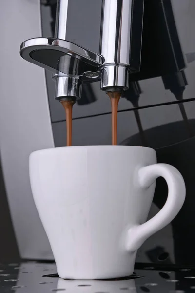 Wake-up coffee espresso with roasted Arabica coffee beans flows under pressure into white Cup. Preparation morning aromatic espresso coffee beans from professional coffee machine. Vertical video.