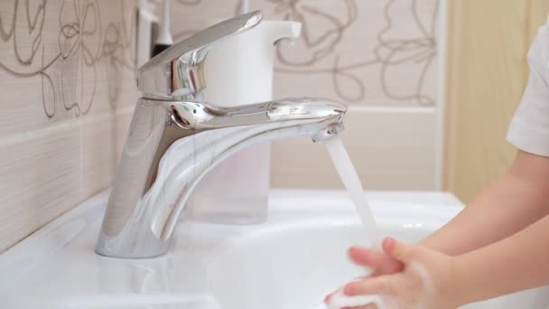 Child picks up soap and foam in his hands brings it to faucet and under water stream washes his hands, closes water in bathroom against background of toothbrushes and bottles close-up — Stock Video