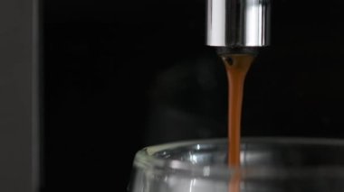 Kavrulmuş Arabika fasulyelerinden gelen kafeinle dolu sıcak, canlandırıcı kahve cam bardağa basınç altında akıyor. Profesyonel kahve makinesinden siyah aromalı kahve çekirdekleri hazırlama.