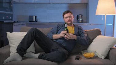 Şişman, tıraşsız, beyaz bir adam evinde dinleniyor ve TV programları veya spor haberleri izliyor. Adam bira açıp kanepede cips yiyor ve akşamları evde film seyrediyor..