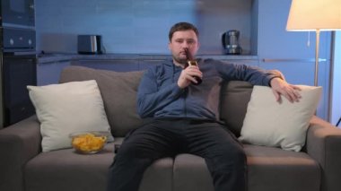 Adam bira içer ve kanepede otururken cips yer, akşamları evde TV 'de film izler. Tıraşsız beyaz adam evinde dinleniyor ve TV 'de TV programları veya spor haberleri izliyor..