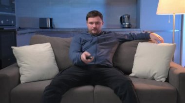 Tıraşsız, yorgun bir adam akşamları kanepede oturur ve zamanını spor programlarını izleyerek geçirir. Uzaktan kumandalı kanalları değiştirir ve televizyondaki haberleri ev mutfağının arka planında seyreder..
