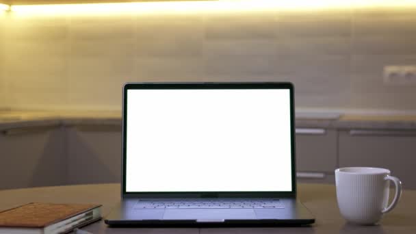 Mock-up asztali elrendezése, számítógép fehér képernyővel és csésze kávé az asztalon otthon a háttérben a konyha. Az otthonról való munkavégzés fogalma. Nagyítsd ki!