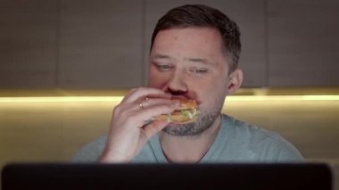 Aç ve tıraşsız bir adam hamburgerden sığır eti yer, akşamları masada dizüstü bilgisayarla oturur ve video bağlantısıyla uzaktan iş arkadaşlarıyla iletişim kurar. Evde uzaktan çalışma.