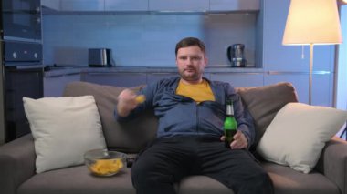 Uykusuzluktan muzdarip bekar şişman bir adam TV kanallarını değiştiriyor, kanepede uzanıyor ve oturma odasındaki koltukta alkollü bira ve patates cipsi içiyor. Adam akşamını evde TV karşısında geçiriyor..