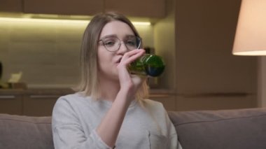 Gözlüklü, yeşil cam şişeden hafif bira içen ve patates cipsi yiyen güzel bir kız portresi. Kadın akşamları evde televizyon izlerken gülüyor ve cips yerken bira içiyor..