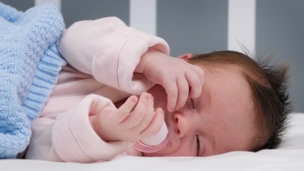 Bebê recém-nascido em macacão creme está dormindo pacificamente na cama no colchão coberto com manta azul e chupando a chupeta. A criança está chorando enquanto dorme. Protecção da criança e criança. — Vídeo de Stock