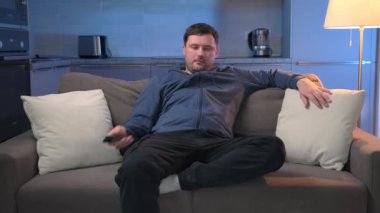 Kafkasyalı, siyah saçlı, traşsız bir adam zor günler geçirdikten sonra evinde dinleniyor, televizyon izliyor, karanlık akşam odasındaki kanepede uzanıyor. TV 'de TV programı izliyorum..