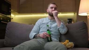 Uzaktan kumandalı bir adam TV kanallarında televizyon programı ya da futbol maçı aramak için takla atıyor. Traşsız adam akşamları haber kanallarını izliyor oturma odasında kanepede oturuyor, bira içiyor, cips yiyor..