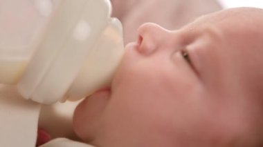  Portre bebek sulandırılmış süt tozu içiyor. Beyaz yeni doğmuş bebek emzik yoluyla küçük plastik bebek şişesinden anne sütü içiyor. Annelik ve çocukluk kavramı. Görüntüleri kapat.